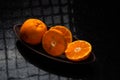 One whole tangerine and one cut in a brown canoe-shaped dish on a black stone table with a window reflection