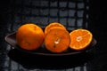 One whole tangerine and one cut in a brown canoe-shaped dish on a black stone table with a window reflection