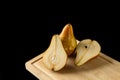 One whole and two halves of a pear on wooden cutting board isolated on black background