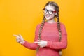 One Winsome Smiling Caucasian Blond Girl In Coral Knitted Sweater Posing In Glasses While Showing Pointing Direction With Both Royalty Free Stock Photo