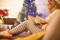 One woman alone at home sitting on the sofa eating cookies and drinking tea or coffe the christmas day - christmas tree at the