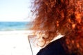 Woman with bright curly red hair by the ocean looks at her mobile phone Royalty Free Stock Photo