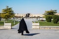 One woman in a chador walks down the Naqsh-e Jahan Square. The black chador waving in the wind. Back view