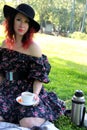 one woman sits on a green hillock, with a white mug and saucer in her hand