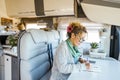 One woman sitting inside modern motorhome alternative tiny house and write travel notes on the table. People living vanlife on the