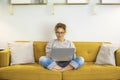 One woman smiling and using laptop computer at home sitting comfortably on a yellow sofa in living room. Smart working female Royalty Free Stock Photo