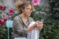 One woman using mobile phone outdoor concentrated with plants and flowers in background. Female writing message on cellphone Royalty Free Stock Photo