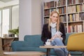 One woman, 40 years old, holding magazine, sitting in book store, book shop, library, shelf full with books behind out of focus Royalty Free Stock Photo
