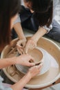 Two women working on a clay bowl on a pottery wheel in a private workshop