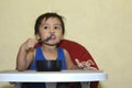 One 1 year old Asian baby boy learning to eat by himself by spoon, messy on baby dining chair Royalty Free Stock Photo