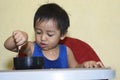 One 1 year old Asian baby boy learning to eat by himself by spoon, messy on baby dining chair Royalty Free Stock Photo