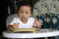 One 1 year old Asian baby boy learning to eat by himself by spoon, messy on baby dining chair Royalty Free Stock Photo