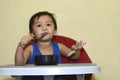 One 1 year old Asian baby boy learning to eat by himself by spoon, messy on baby dining chair Royalty Free Stock Photo