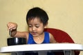 One 1 year old Asian baby boy learning to eat by himself by spoon, messy on baby dining chair