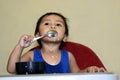 One 1 year old Asian baby boy learning to eat by himself by spoon, messy on baby dining chair at home Royalty Free Stock Photo