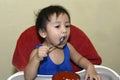 One 1 year old baby boy learning to eat alone messy on baby dining chair at home Royalty Free Stock Photo