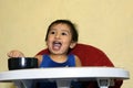 One 1 year old baby boy learning to eat alone smiling happy but messy on baby dining chair at home Royalty Free Stock Photo