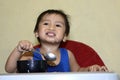 One 1 year old baby boy learning to eat alone smiling happy but messy on baby dining chair at home Royalty Free Stock Photo