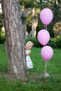 Cute baby girl in a colorful dress hiding behind a tree in the park and smiling Royalty Free Stock Photo