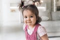 One year old baby is looking at the camera. Baby with two ponytails in a pink sundress. Cute girl sitting on a sofa Royalty Free Stock Photo