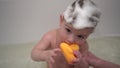 A one-year-old boy bathes in a bathtub with foam on his head. A small child washes with a small rubber duck. Royalty Free Stock Photo