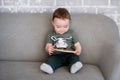 The one-year-old boy is sitting on a gray sofa with a book Royalty Free Stock Photo