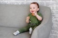 The one-year-old boy is sitting on a gray sofa and smiles happily Royalty Free Stock Photo