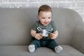 The one-year-old boy is sitting on a gray sofa and smiles happily Royalty Free Stock Photo