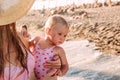 One-year-old cute European baby girl is holding on to her mother on the beach in the summer. Mother and daughter in pink swimsuits