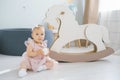 A one-year-old girl in a pink dress holds a white ball in her hands and sits next to a rocking horse toy Royalty Free Stock Photo