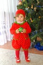 The one-year-old girl in a suit of strawberry stands near a New Year tree Royalty Free Stock Photo