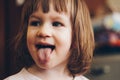 A one-year-old smiling girl sits at a children`s table in a high chair and eats with a spoon from a bowl. Colored background. Royalty Free Stock Photo