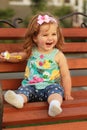 One year old sweet girl sitting on a wooden bench and laughing out load