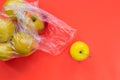 One yellow apple rolled out of plastic bag with apples on oral background.