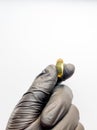 One yellow capsule of fish oil in hand in a black medical glove on a white background. Hand with pills on a white background Royalty Free Stock Photo