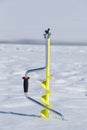 One yellow ice drill auger stuck in the snow on a frozen lake
