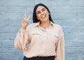 One young business woman of indian ethnicity standing outside against a grey wall and gesturing the peace sign with her Royalty Free Stock Photo