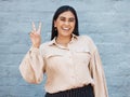 One young business woman of indian ethnicity standing outside against a grey wall and gesturing the peace sign with her Royalty Free Stock Photo