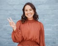 One young business woman of mixed race ethnicity standing outside against a grey wall and gesturing the peace sign with Royalty Free Stock Photo
