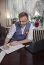 One young businessman sitting in his apartment, writing in notebook, laptop on table Royalty Free Stock Photo