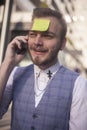 One young businessman, talking on a phone, with sticky note glued to his forehead Royalty Free Stock Photo