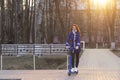 One young Caucasian woman with red hair in a blue coat quickly rolls or rides a blue electric scooter in the park. Eco Royalty Free Stock Photo