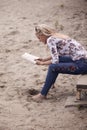 One young girl, sitting on steps on beach sand, summer, happy smiling, reading a book outdoors. side view