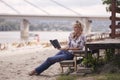 One young girl, sitting on steps on beach, summer, happy smiling, reading a book outdoors. side view