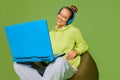 One young girl, student wearing headphones and holding laptop on knees looking at screen and smiling over green Royalty Free Stock Photo