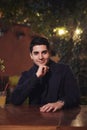 One young handsome man portrait, sitting in cafe garden at table, night outdoors, looking to camera. upper body shot Royalty Free Stock Photo