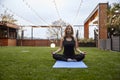 One young lady, 20-29 years old, meditating in a backyard of a fancy house with a beautiful view on mountains. sitting on yoga mat