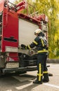 One young male firefighter dressed in uniform with protective helmet near fire engine.