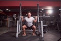 One young man, barbell back squat, dark gym indoor. full lenght