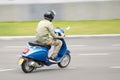 One young man in camouflage clothes riding fast blue scooter on